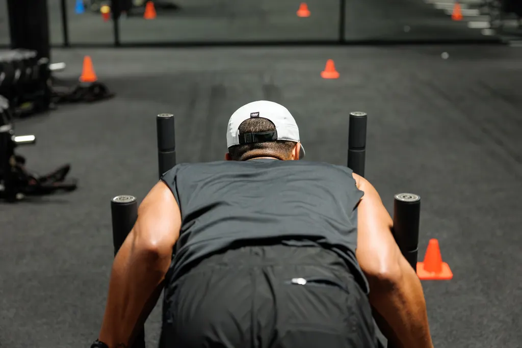 Athlete driving a weighted sled down the turf lane during HYROX training at Dallas Performance Systems