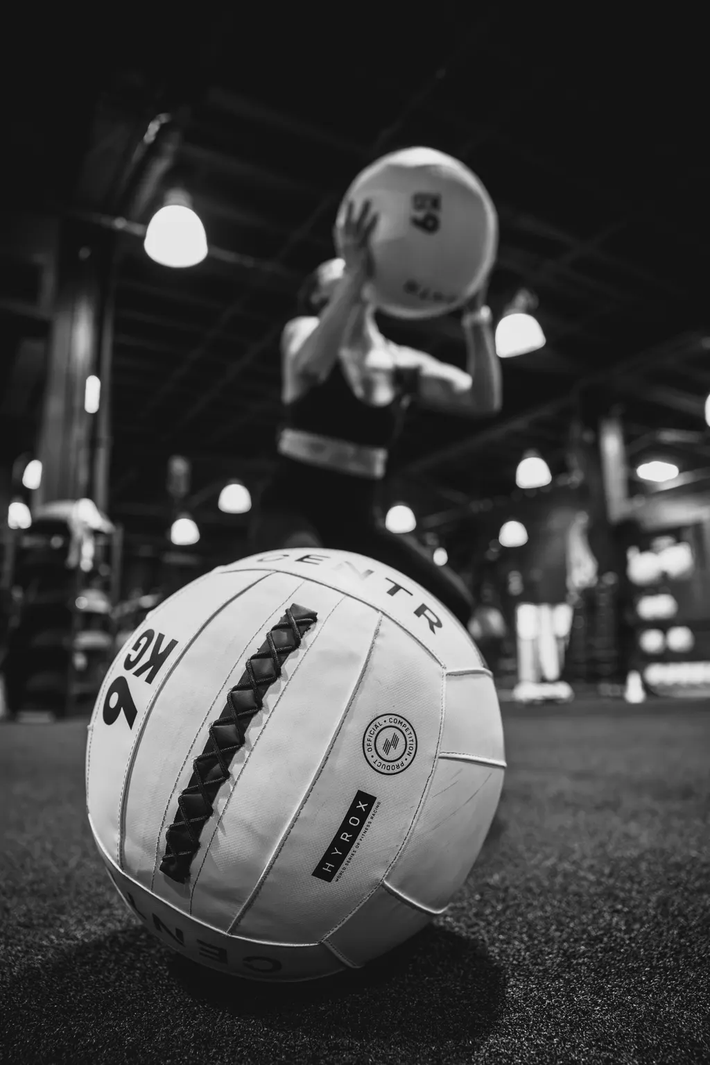White HYROX wall ball on the turf as an athlete throws in the background at DPS